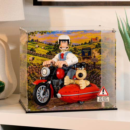 Wallace and Gromit LEGO set 21371 inside a clear acrylic display case with a printed countryside background, on a white sideboard