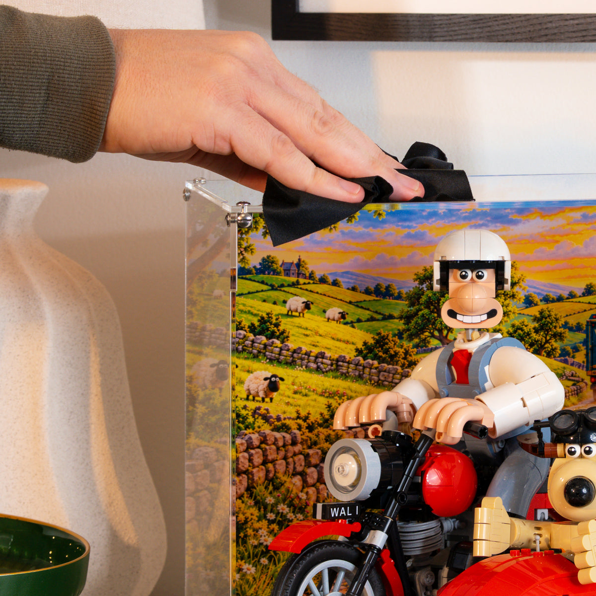 A hand wiping the acrylic case with a cloth, with Wallace and Gromit inside